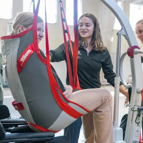 Students help a Maine Adaptive client into a power wheelchair using a lift